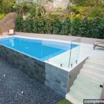 floating blue pool with sandstone paving and glass side