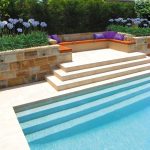 Modern pool corner with sandstone wall and flowers