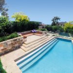 A modern pool with descending steps along the way surrounded by a garden