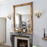 A gold-framed mirror sitting atop a stone fireplace is a throwback to ’40s perfection