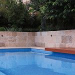 A modern pool next to a wall and a bench