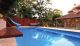 A modern blue pool next to a house with outdoor furniture and a water slide