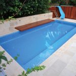 A modern blue pool with a water slide and outdoor furniture surrounded by plants