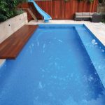 A blue pool with a wooden bench and a water slide