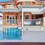 outdoor tropical-inspired landscape with frameless fencing and pergola
