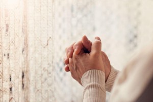 hands praying near a curtain windows