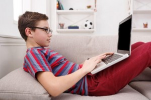 teenage boy using laptop for web surfing while lying on the couch