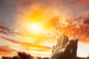Hands together praying in bright sky