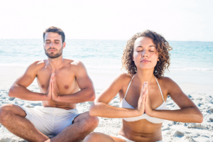 happy couple doing yoga beside the water at the beach