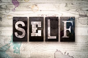 The word "SELF" written in vintage dirty metal letterpress type on a whitewashed wooden background with ink and paint stains.