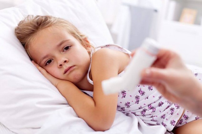 sick litle girl lying on bed with asthma puffer given to her