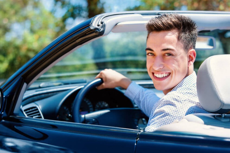 Young man sitting in convertible in driver seat.