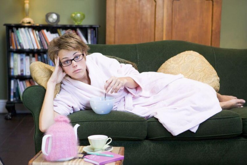 Young woman lying on sofa at home eating a sweet treat