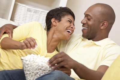 Save Download Preview A happy African American man and woman couple in their thirties sitting and laughing eating popcorn