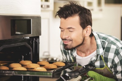 smiling man sniffing baked cookies from an oven